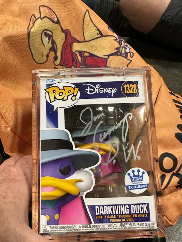 Darkwing Duck Funko pop with silver signature of Jim Cummings with gold backpack in background with Morkor the Kobold on it.