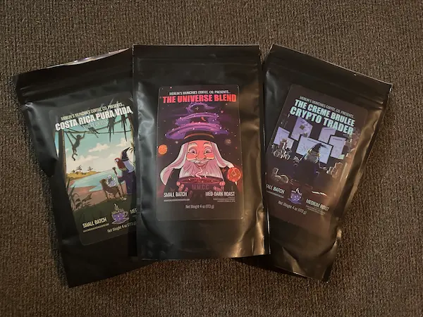 Three black bags of coffee. First one called Costa Rica Pura Vida. Second with wizard called the Universe Blend. Third called the Creme Brulee Crypto Trader.